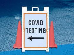 sign in front of two orange cones that says COVID TESTING with a left arrow beneath it