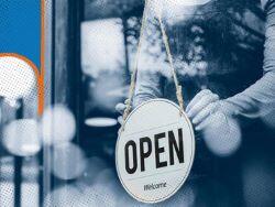 person hanging an "open" sign inside a glass door